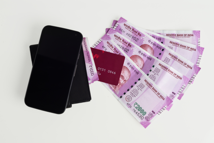 Top view of new Indian Currency notes of 2000 rupee with Mobile phone, wallet and credit cards. All articles are in sharp focus in white background. You could add your own content on the blank screen of the mobile phone.